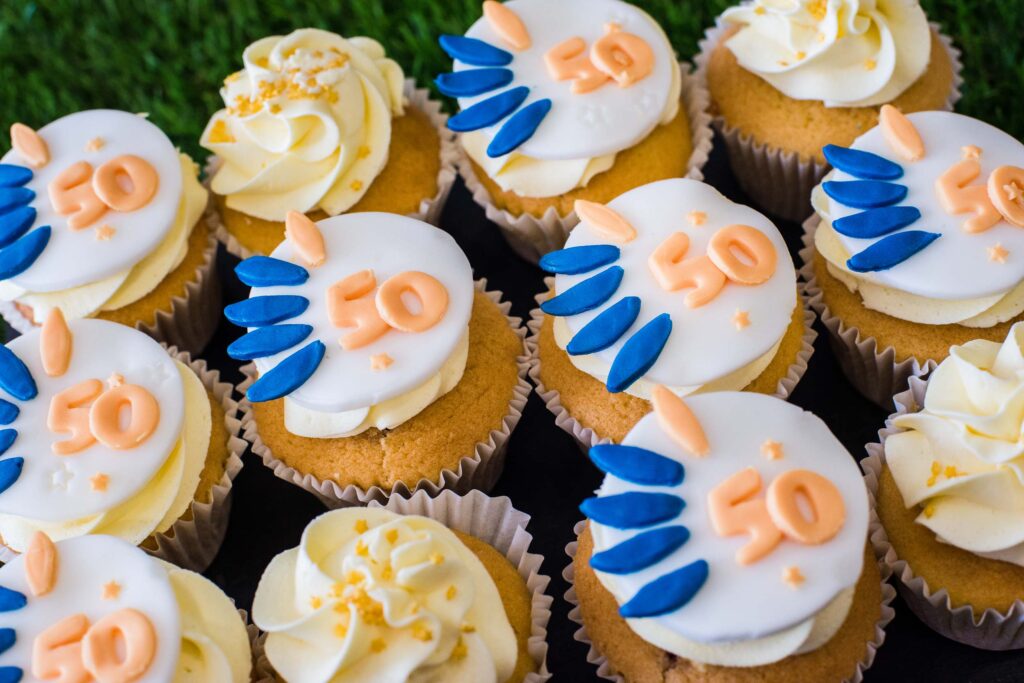 Disability Wales 50th anniversary cupcakes. They have white icing with the DW blue and orange 50th anniversary logo on them.