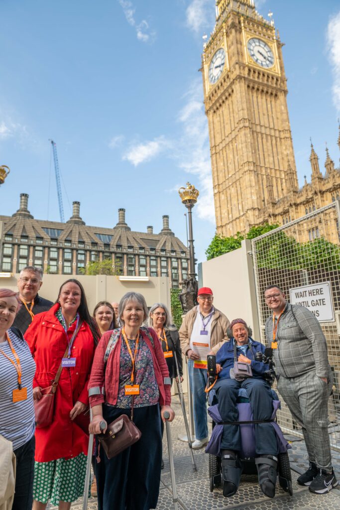 DW staff and members standing in front of Big Ben in London on a sunny day. They all attended the Mass Lobby against disability benefit cuts.