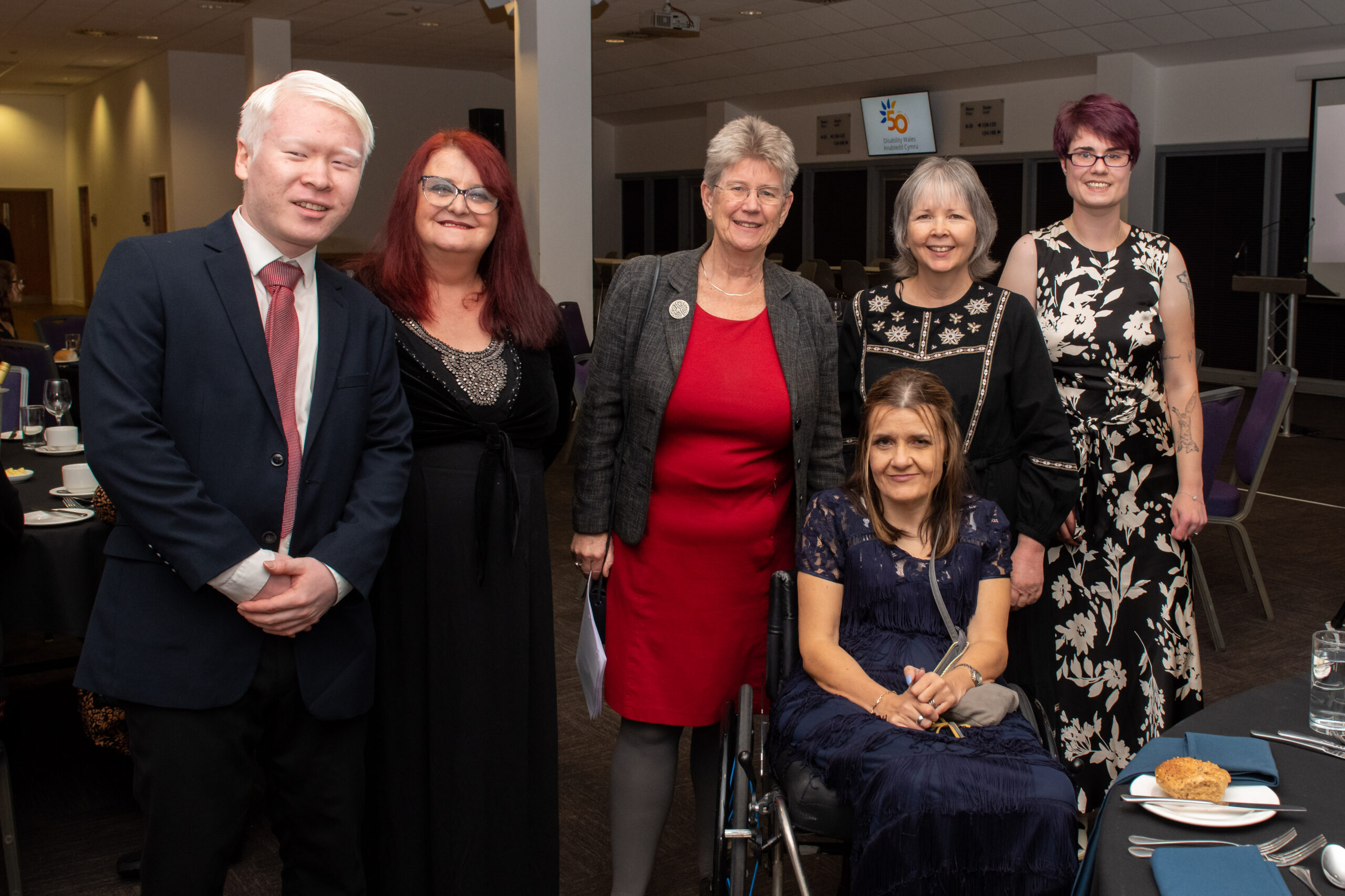 DW staff and board members with Jane Hutt MS, Minister for Social Justice   Back row: Left to Right: Felix Shi (Director), Willow Holloway (Chairperson), Minister for Social Justice Jane Hutt MS, Rhian Davies (Chief Executive), Alex Osborne (Disability Equality Officer) Front: Anne Champ (Vice Chairperson). They're all smiling and wearing smart clothes ready to celebrate at DW's 50th anniversary dinner.