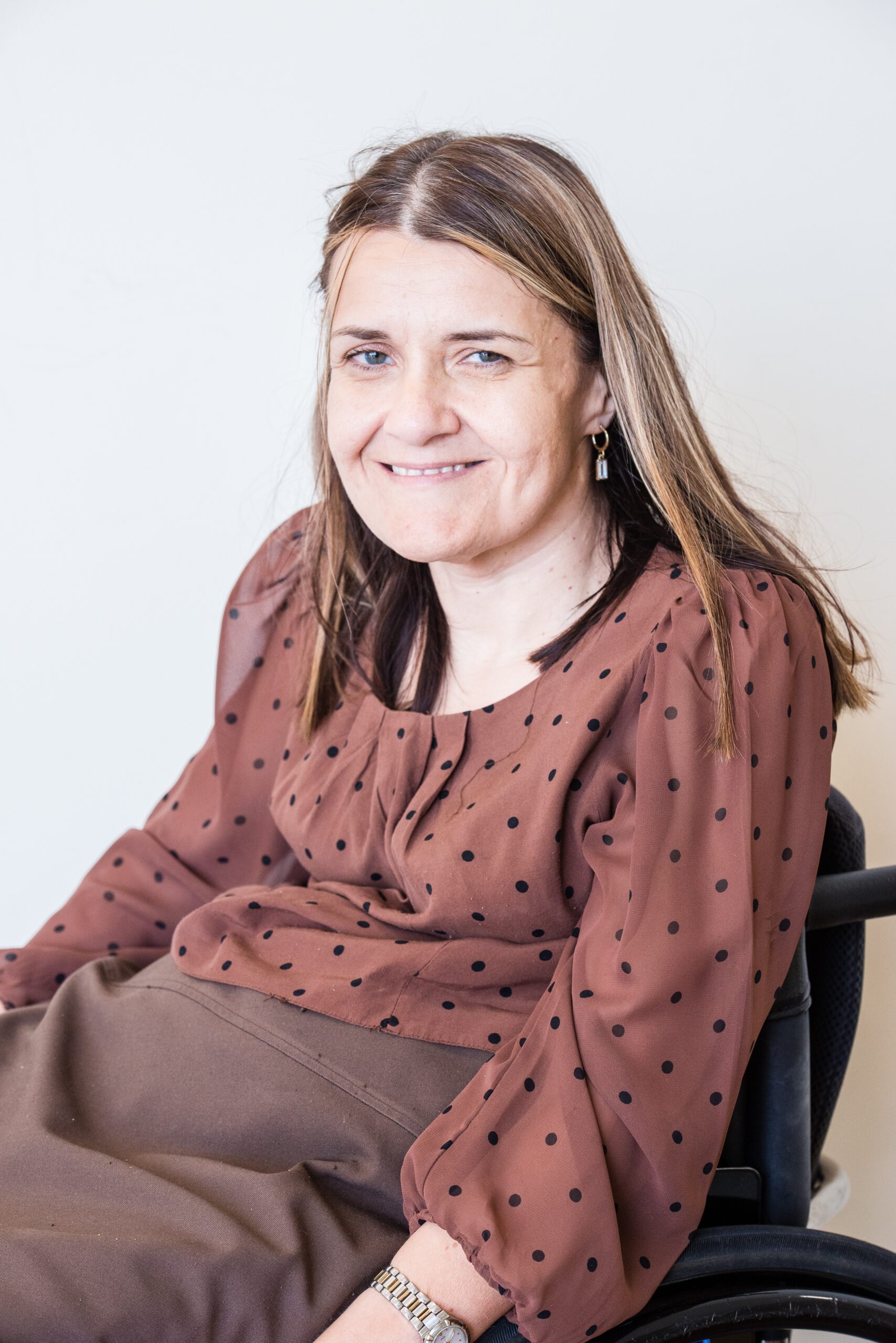 Board member Anne smiling at the camera. She has long brown hair which is parted in the centre and she wears a brown dress with black polka dots.