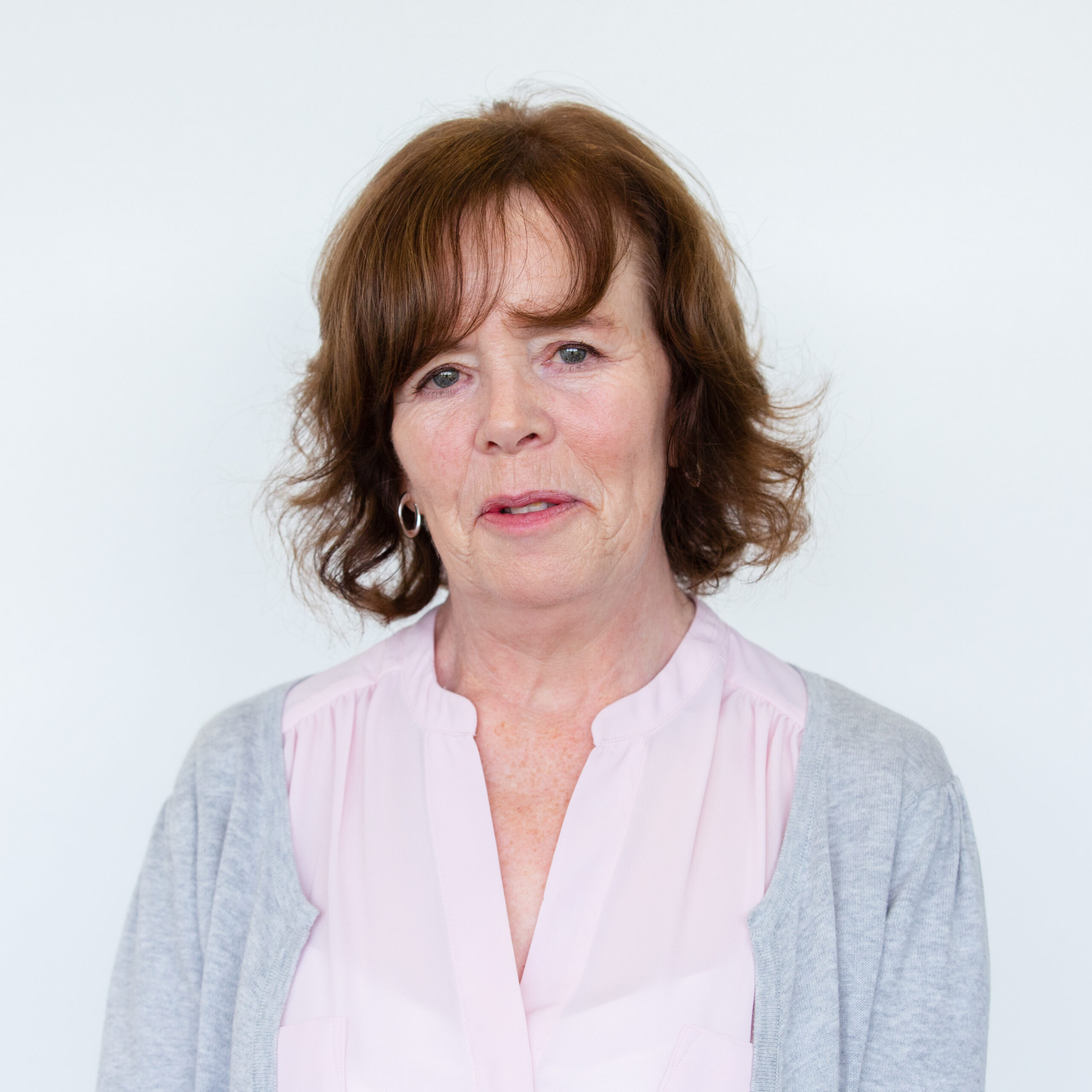 Tracey Blockwell in front of a plain white wall. She has short, slightly curled dark hair