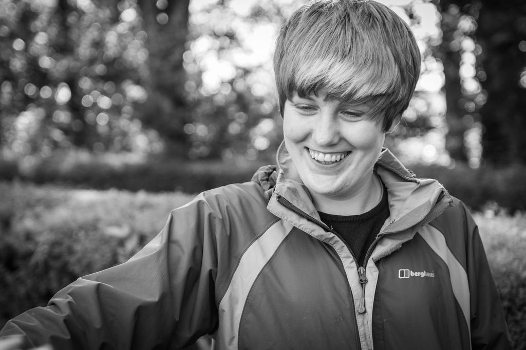 A black and white photo of our dear friend and former colleague, Becky Newsome, who smiles broadly. There are trees in the background.